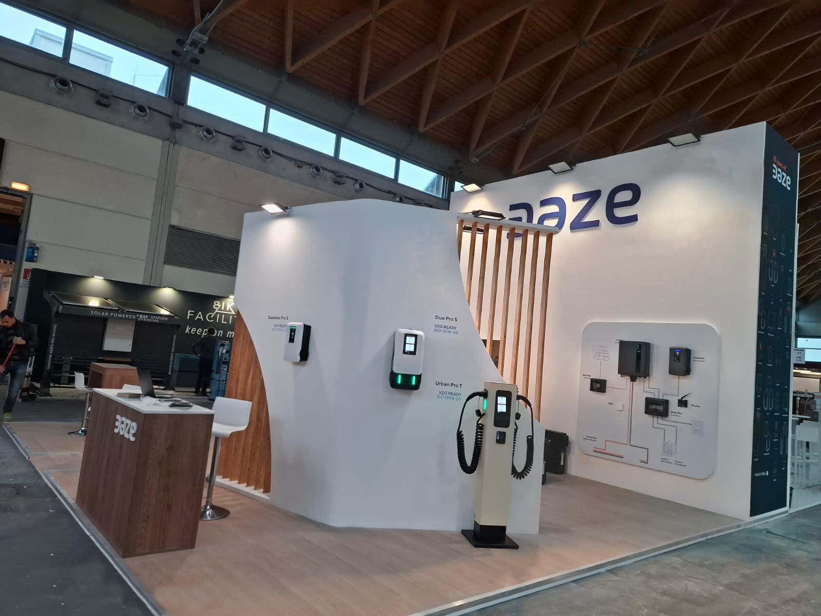 Parete curva con wallbox e colonnina di ricarica, sullo sfondo il grande logo 3D Daze