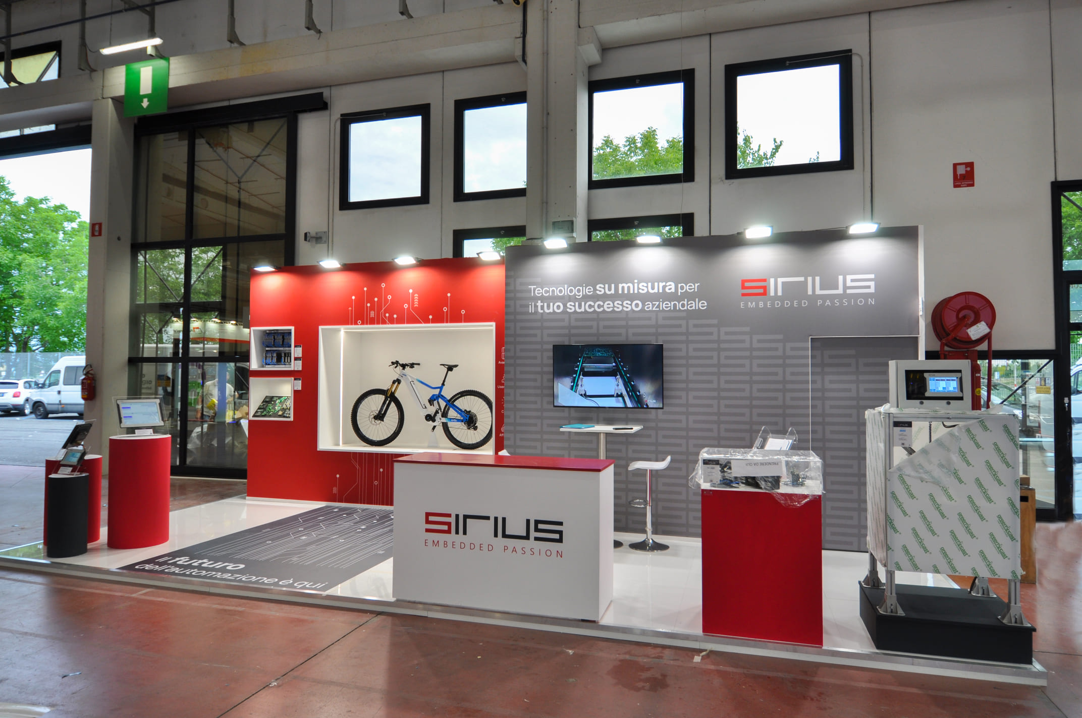 Vista frontale dello stand Sirius dalla corsia: bancone logato, vetrina e macchinario in esposizione