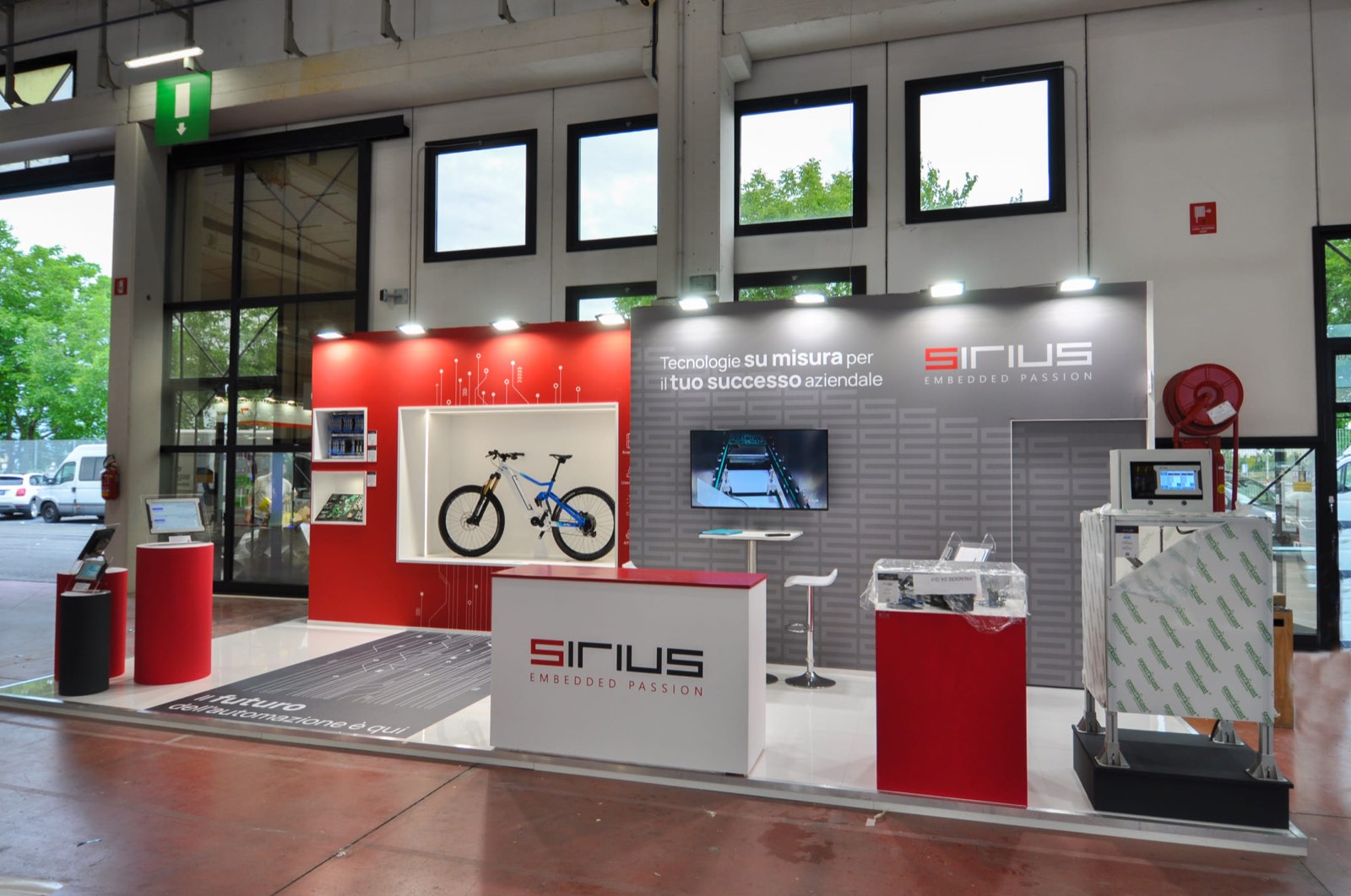 Vista frontale dello stand Sirius dalla corsia: bancone logato, vetrina e macchinario in esposizione